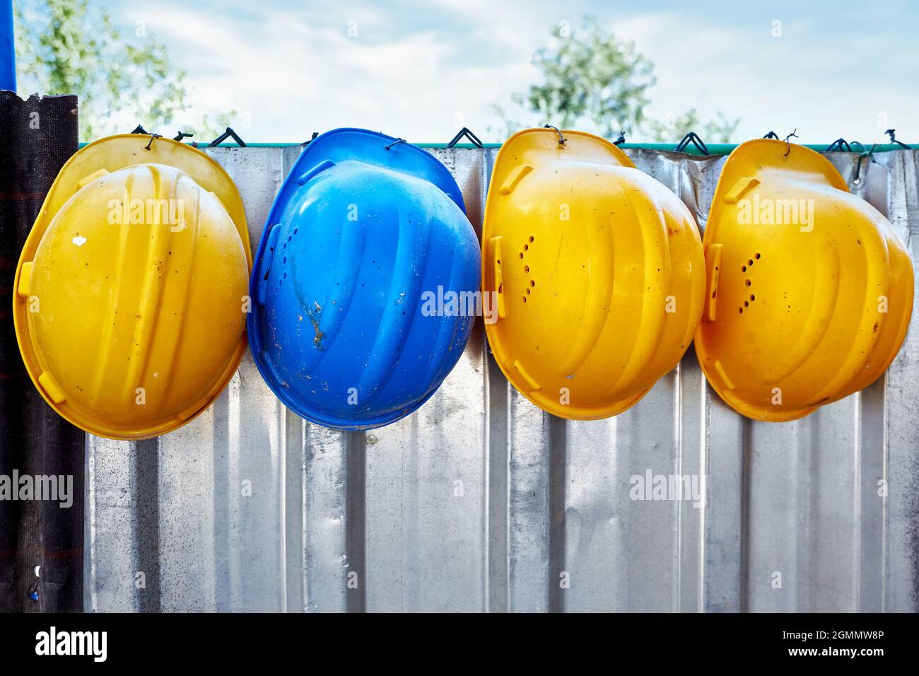 Safety hats hanging on a metal fence in a row at the construction site