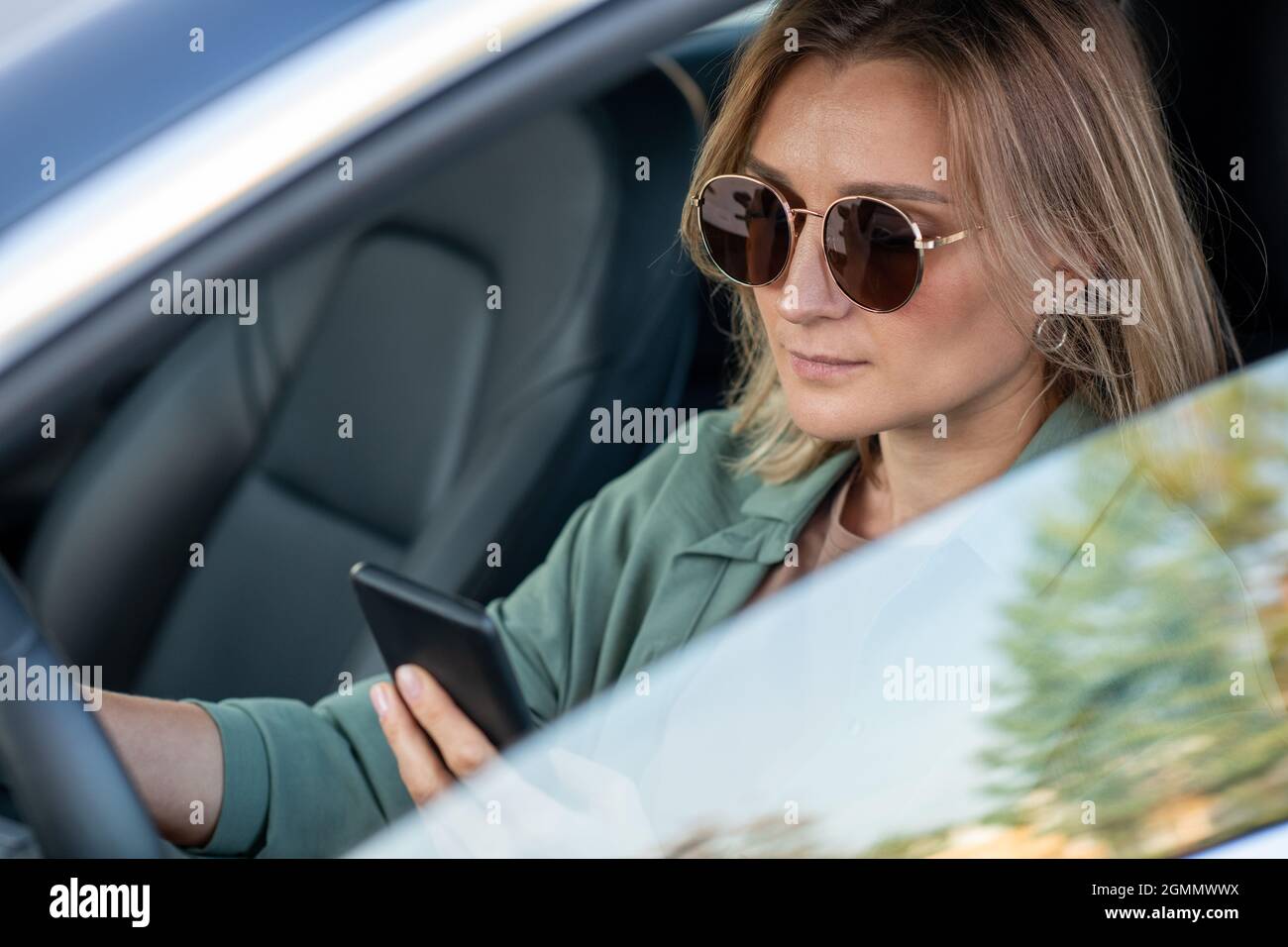 Young contemporary woman driving car and texting in smartphone in the morning Stock Photo