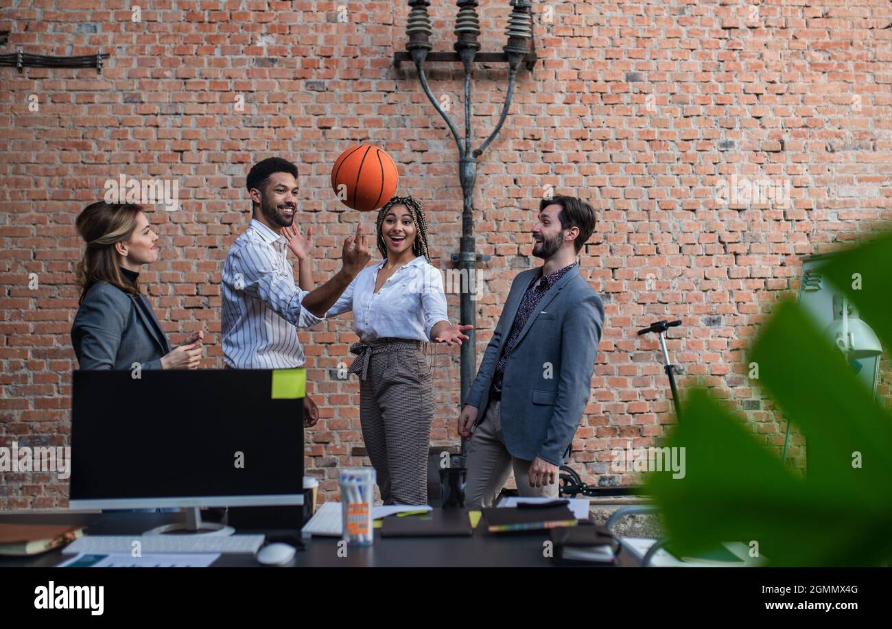 Group of cheerful young businesspeople playing basketball in office, taking a break. Stock Photo
