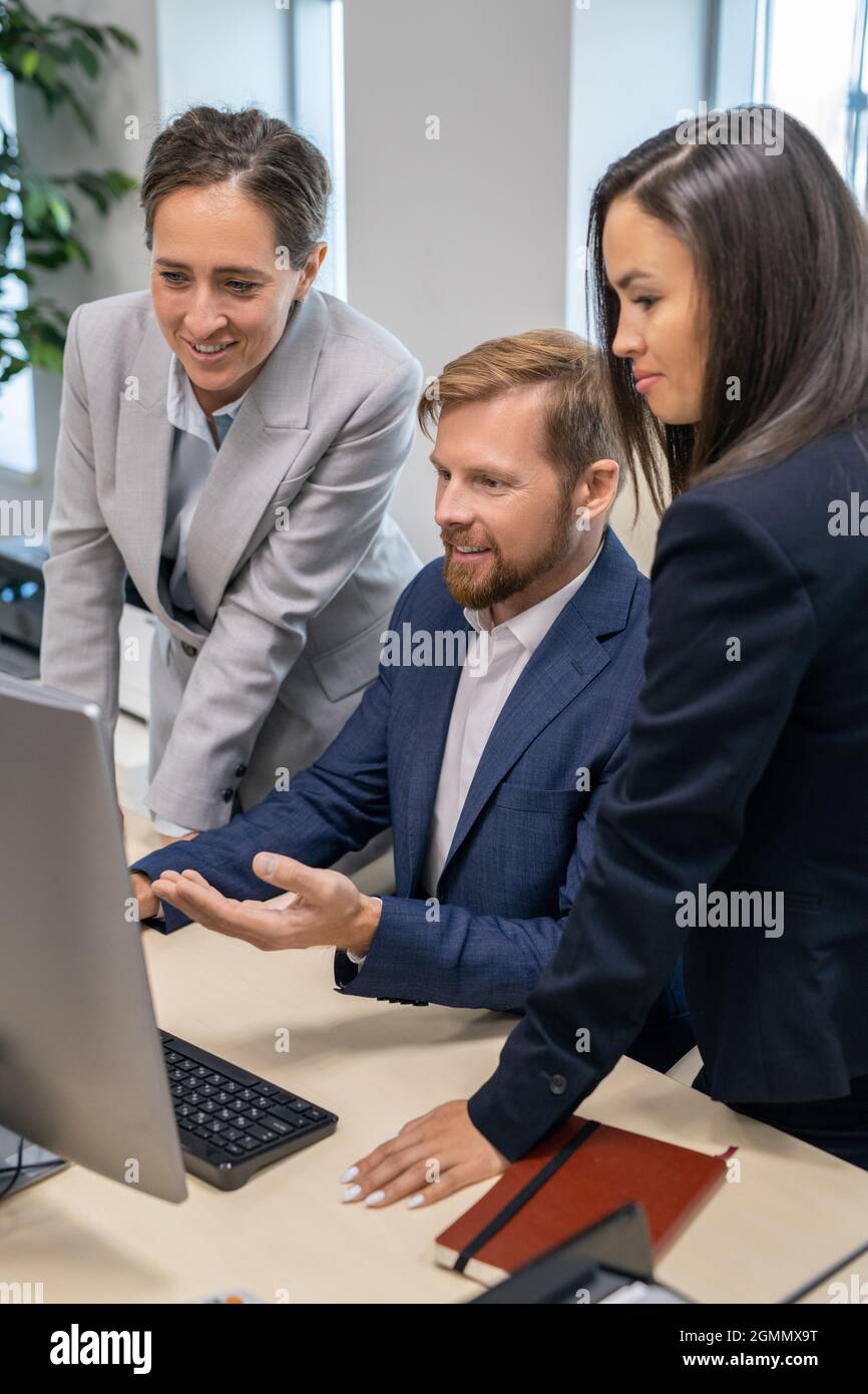 Three young office workers in suits looking at computer screen during presentation Stock Photo