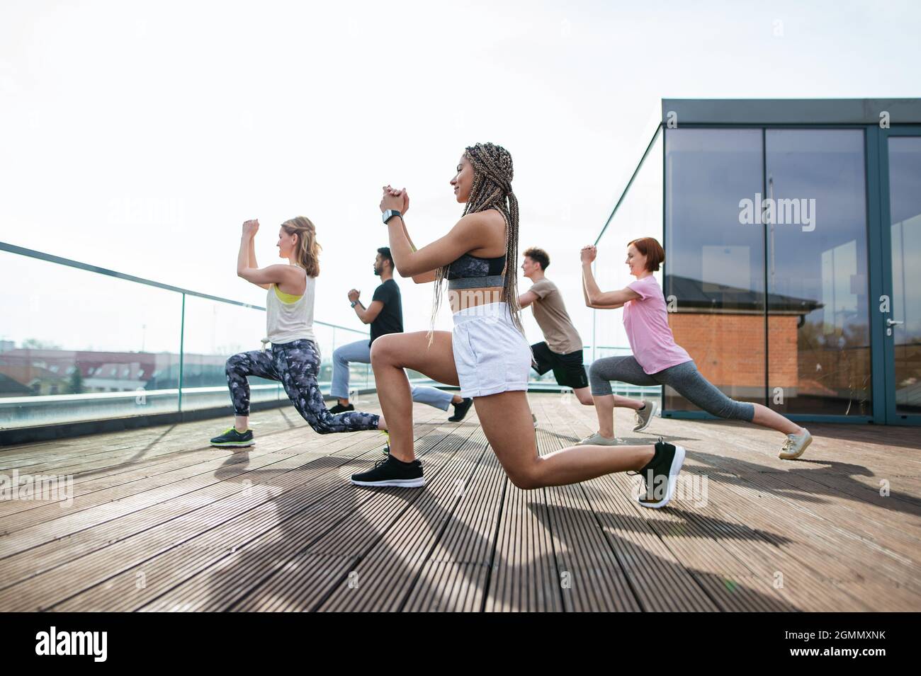 Group of young people doing exercise outdoors on terrace, sport and healthy lifestyle concept. Stock Photo