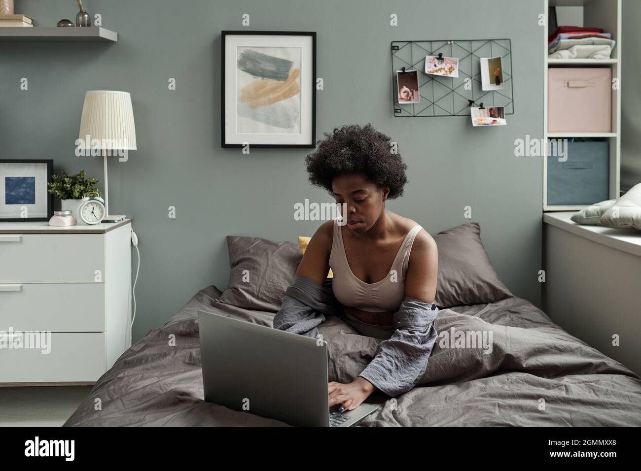 Young serious female looking at laptop screen while sitting on bed after sleep Stock Photo