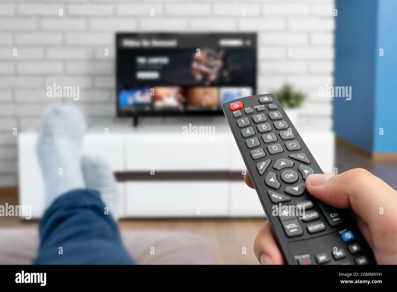 Man watching TV, lying on sofa, legs on table. Person holding remote control in living room Stock Photo