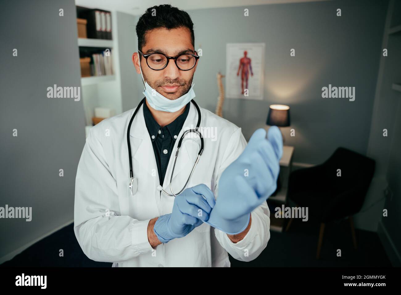 Mixed race male doctor working in office preparing for appointment putting surgical gloves on Stock Photo