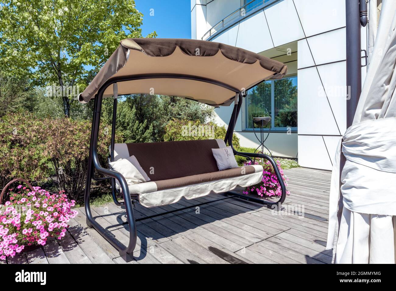 Garden canopy swing bench on wood paved patio area in country estate garden in summer Stock