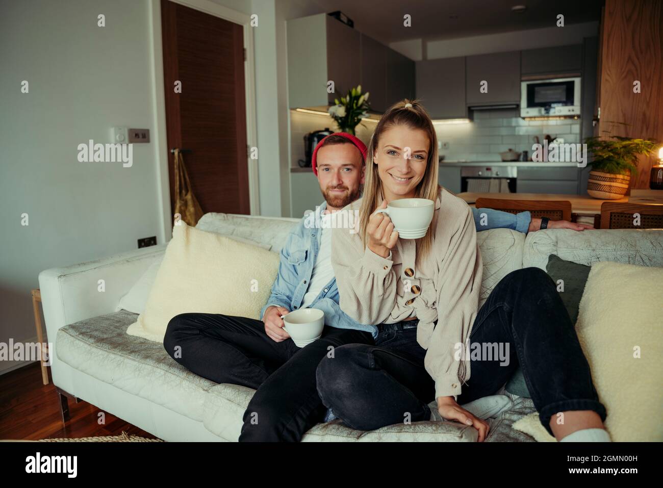 Caucasian couple sitting on couch drinking coffee happily  Stock Photo
