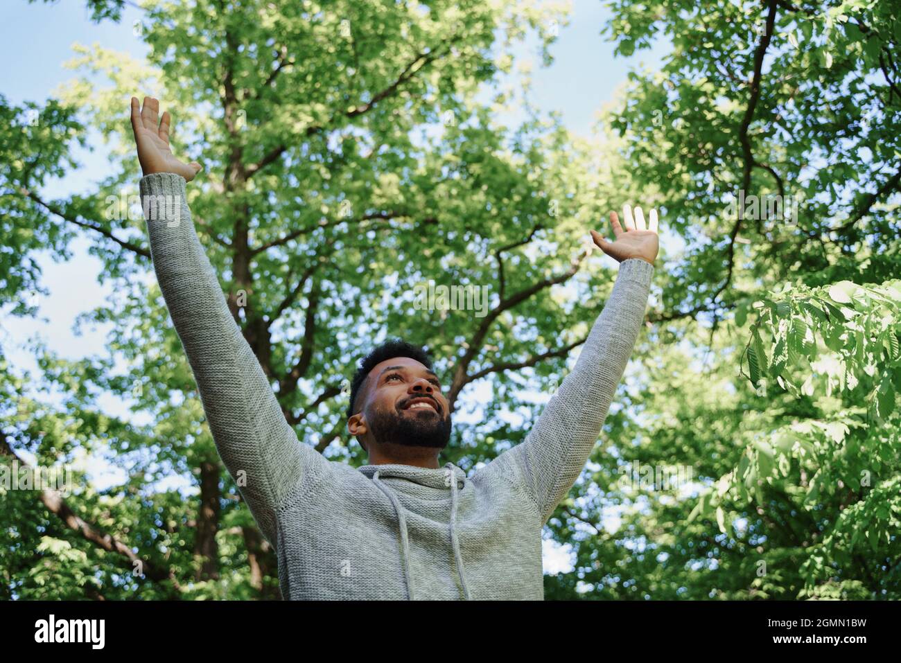 Low angle view of happy young man doing stretching exercise outdoors in forest, weekend away and digital detox concept. Stock Photo