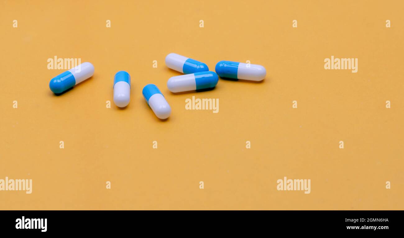 Blue-white capsules pill on yellow background. Pharmacy banner. Capsule pills manufacturing industry. Pharmaceutical industry. Drug development. Stock Photo