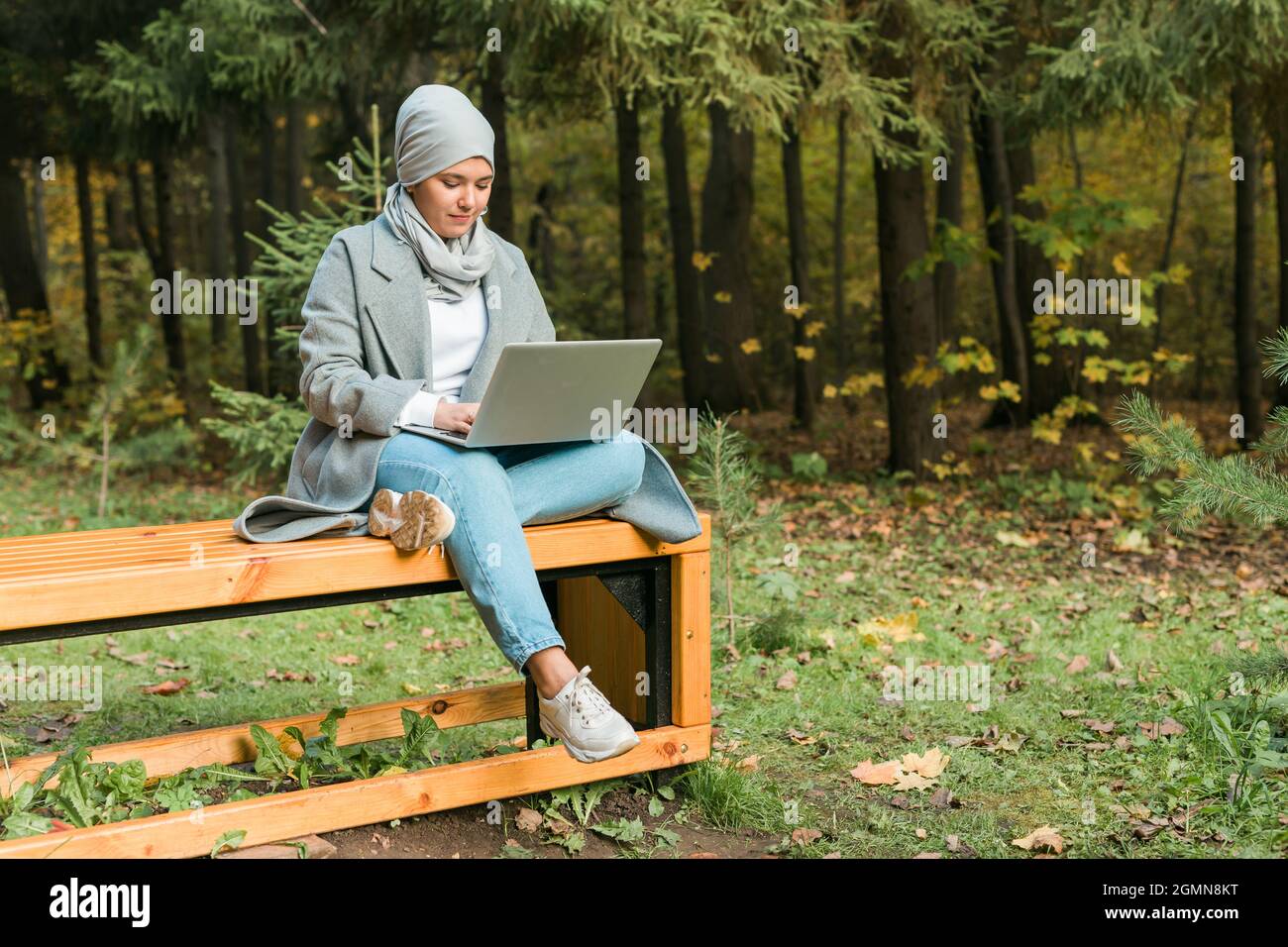 Young asian muslim woman using laptop at autumn park. Online education ...