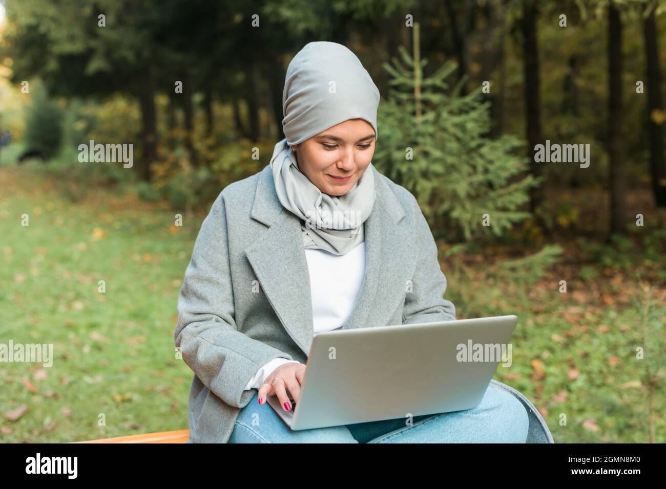 Young asian muslim woman using laptop at autumn park. Online education ...