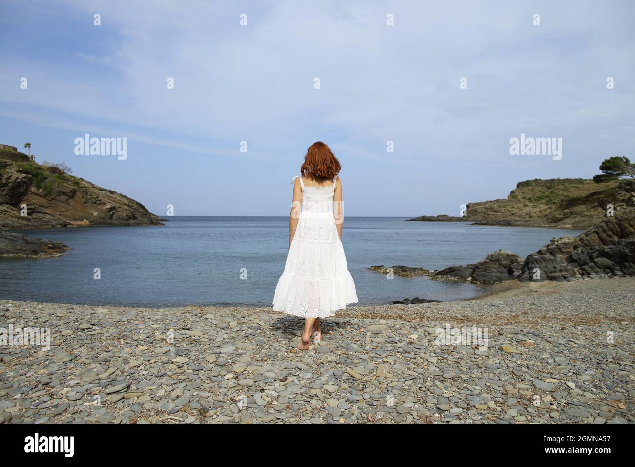 Back view full body portrait of a woman walking towards water contemplating views on the beach Stock Photo