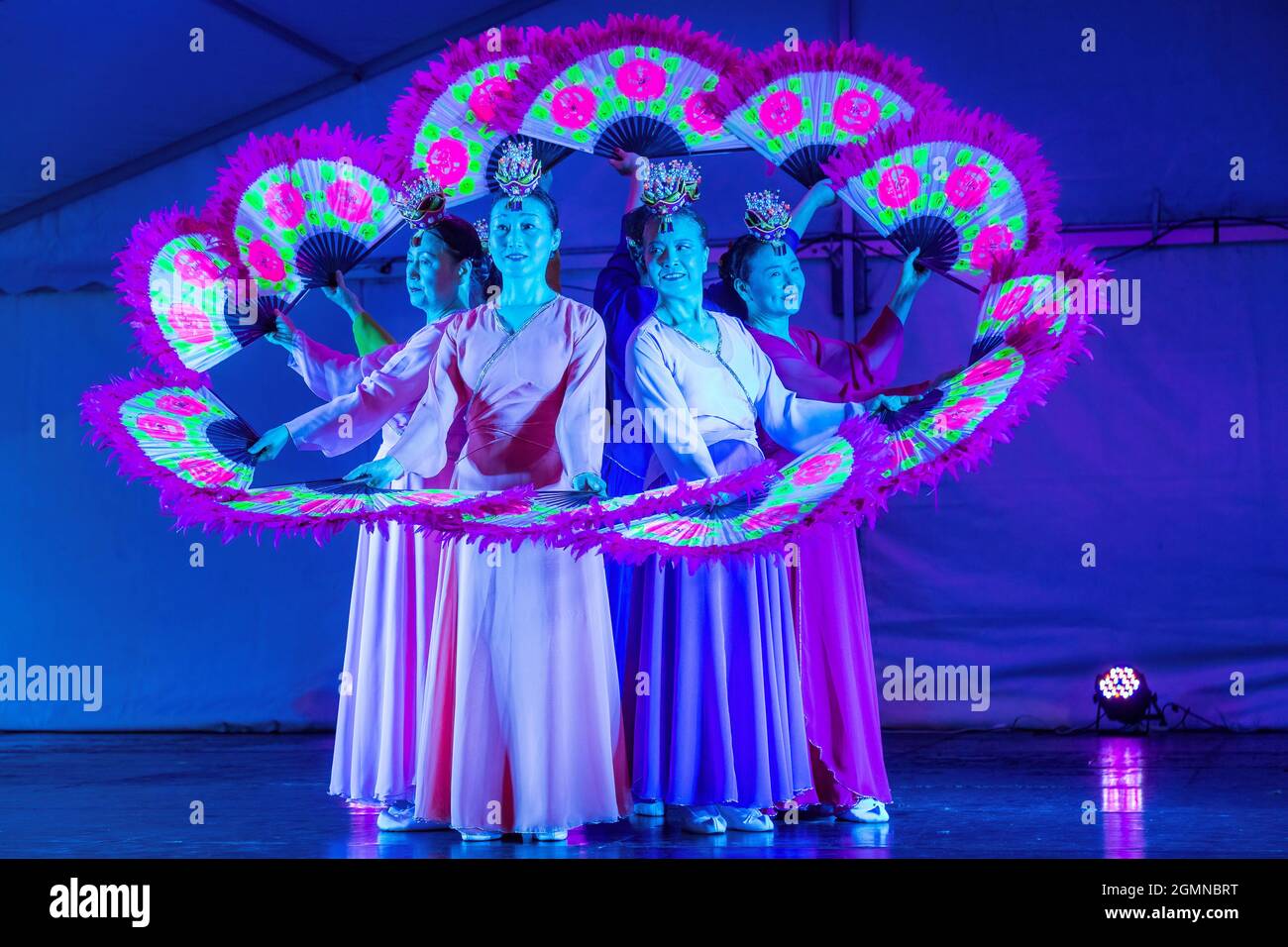 Korean women performing a buchaechum, or traditional fan dance, on stage under artificial lighting. They are wearing hanbok dresses Stock Photo