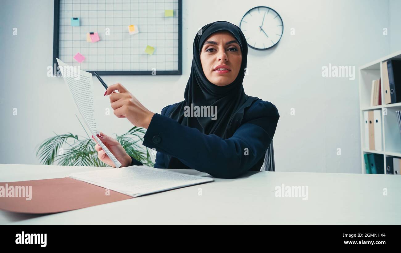 muslim woman in hijab pointing with pen at document in modern office ...