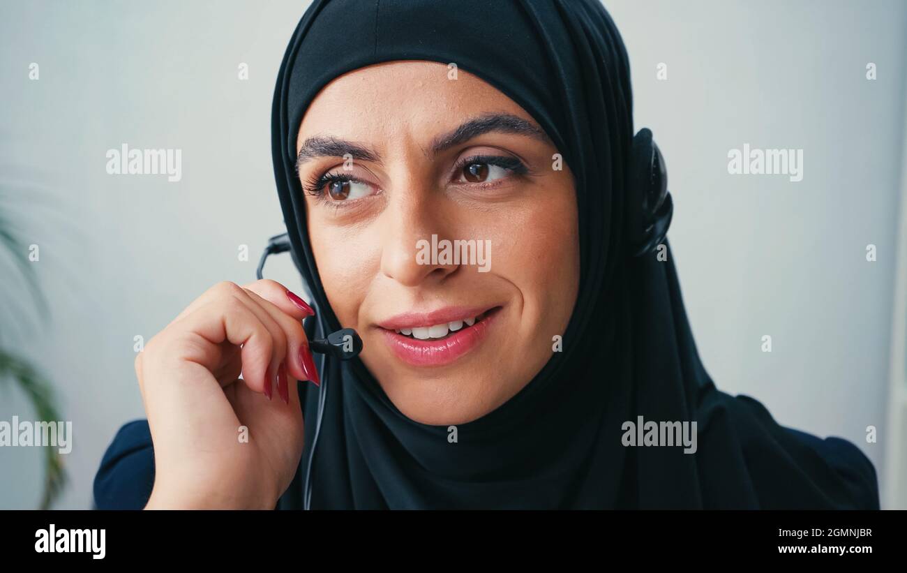 Muslim operator of call center using headset and smiling in office ...