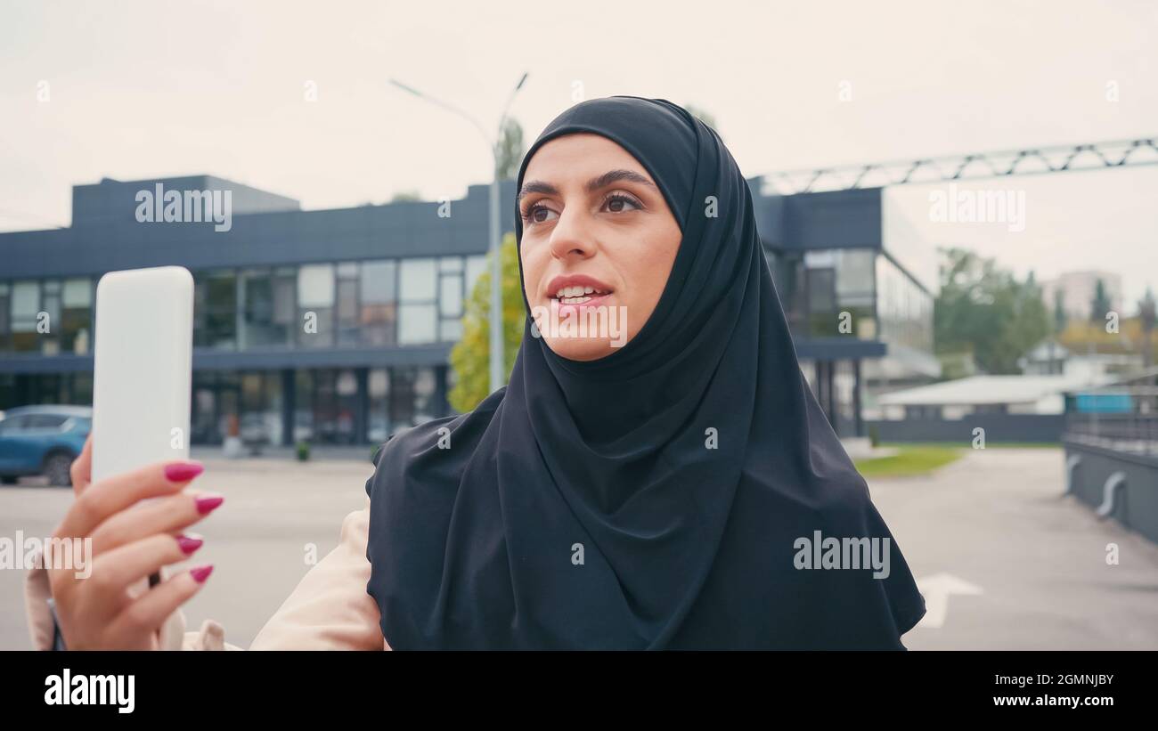 Young muslim woman in hijab talking while having video call on urban ...