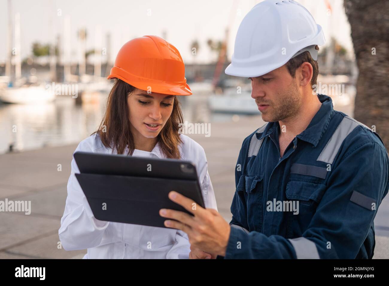 Serious male engineer and female inspector in hardhats discussing information on tablet during meeting in sea port Stock Photo