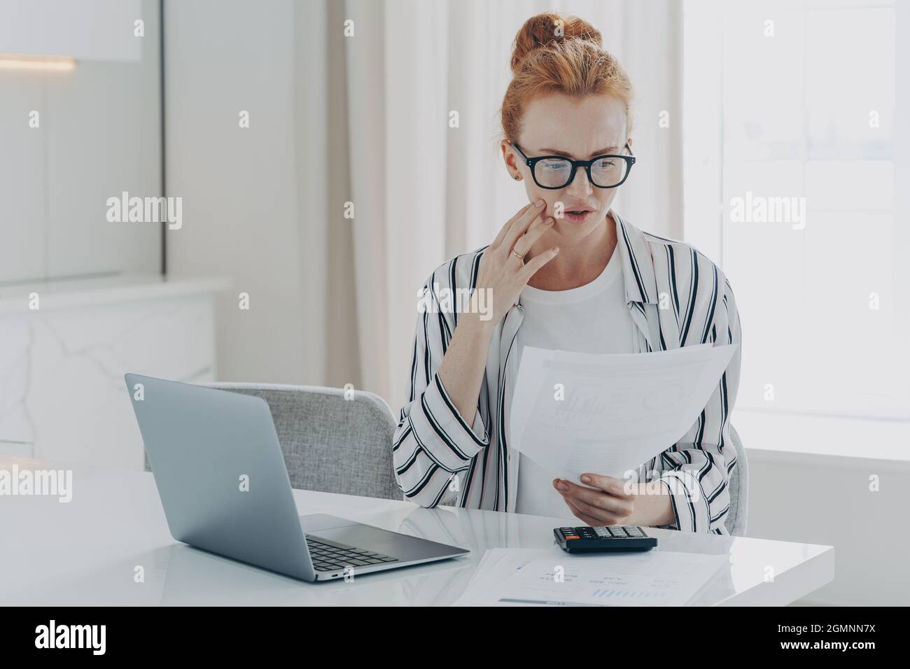 Young depressed woman with having financial problems, sitting at table with laptop and calculator Stock Photo