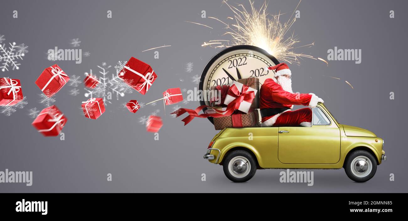Christmas is coming. Santa Claus on toy car delivering New Year 2022 gifts and countdown clock at gray background with fireworks Stock Photo