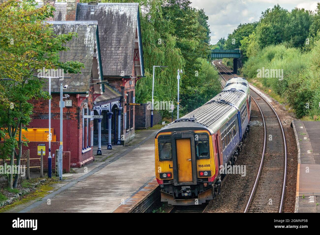 Class 156 diesel multiple unit train passing through rural station. Stock Photo
