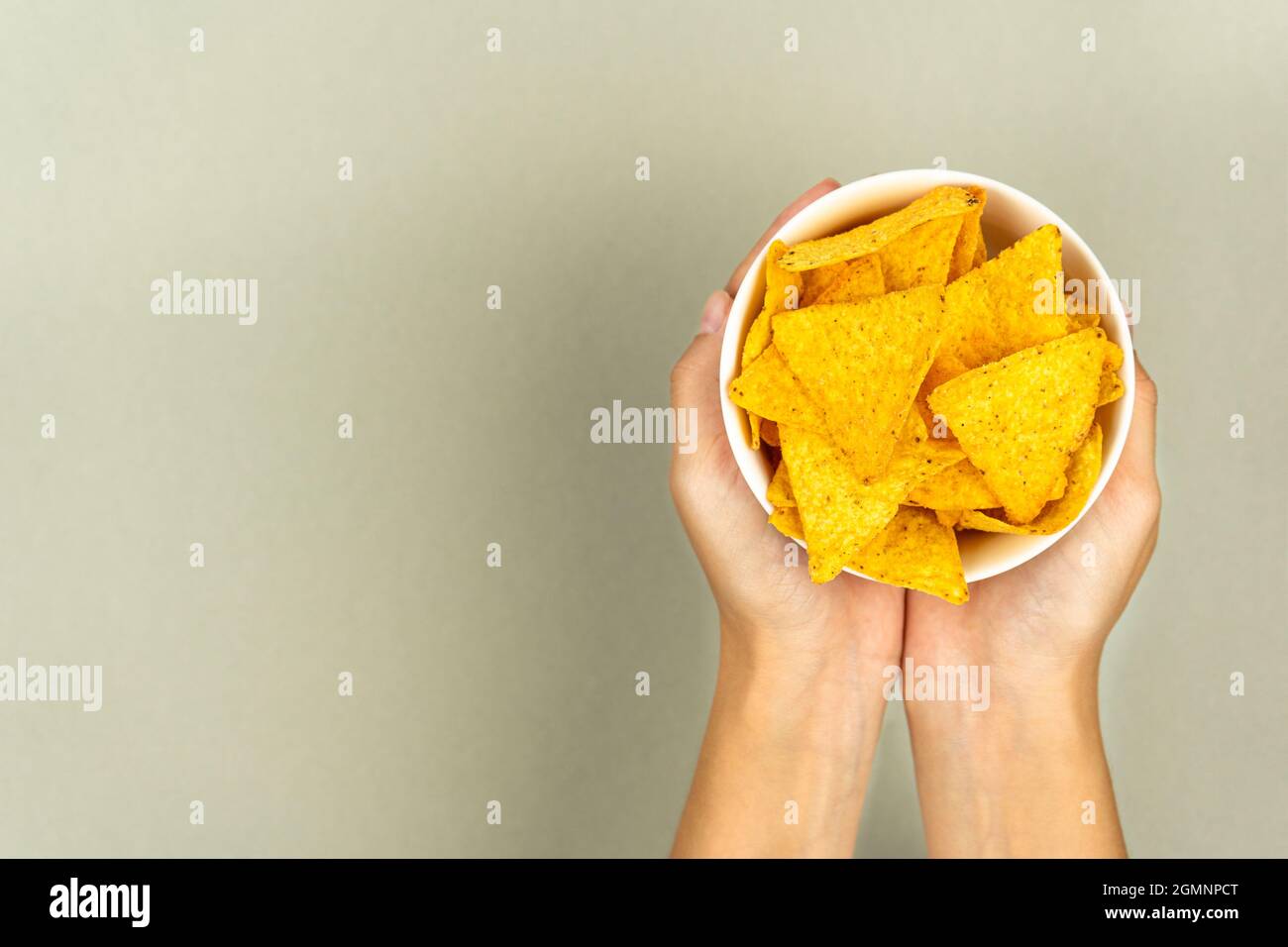 Treating crispy nachos chips in a plate and female hands on a colored