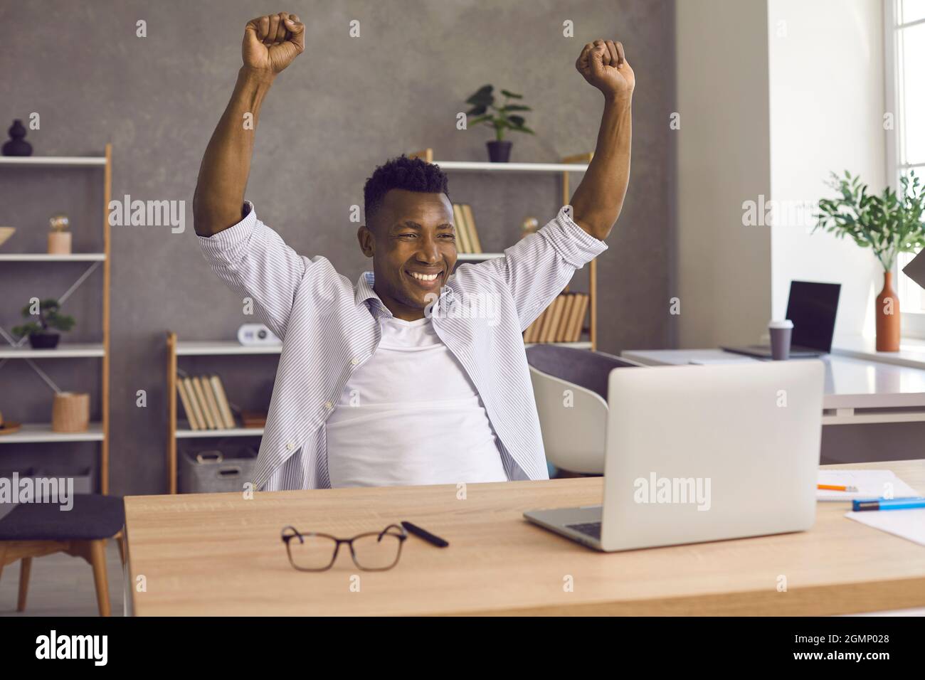 Dark-skinned man happily raises his hands after receiving good news or achieving desired goal. Stock Photo