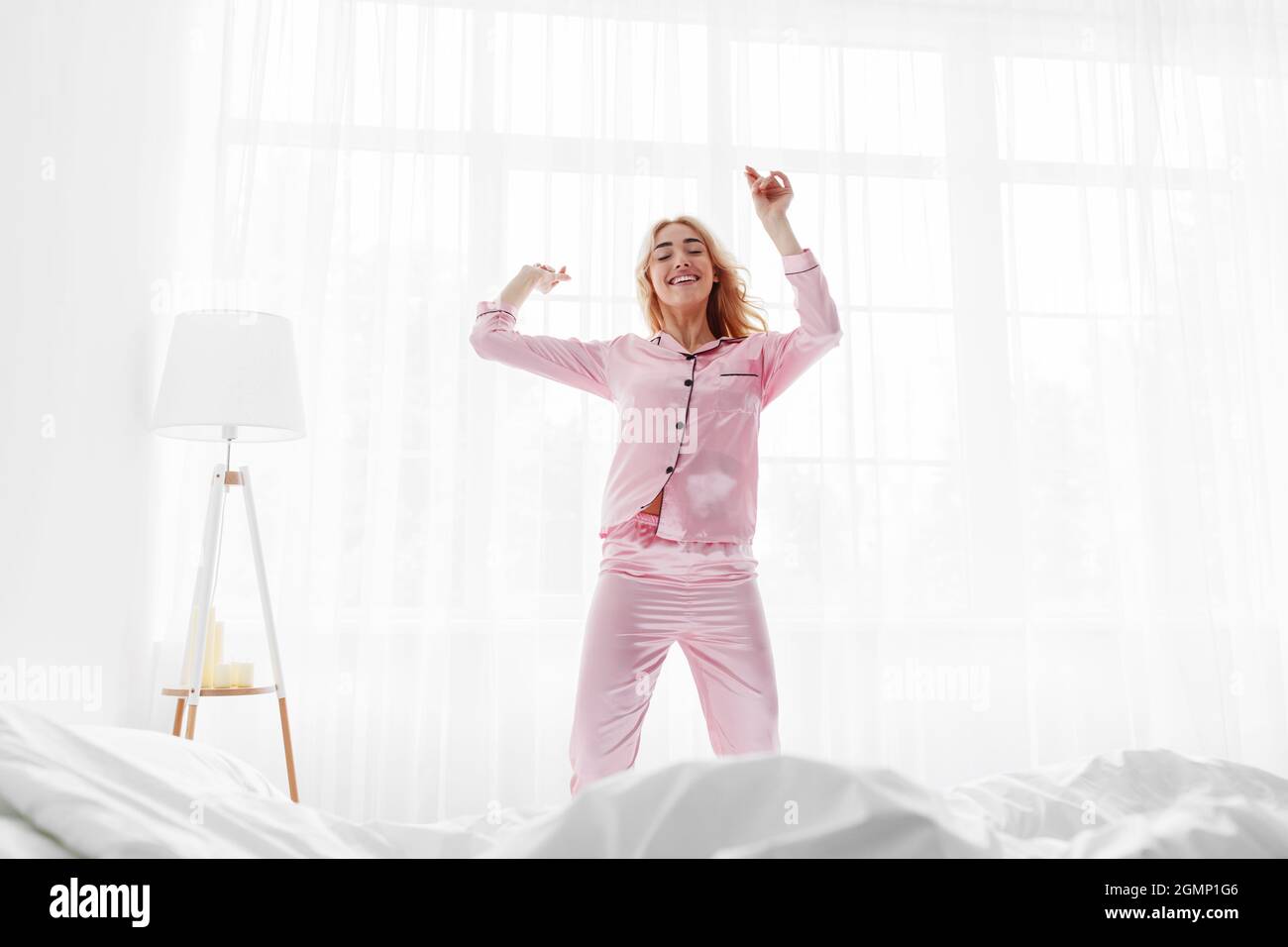 Happy young european blonde female in pink pajama dancing and enjoys good morning Stock Photo