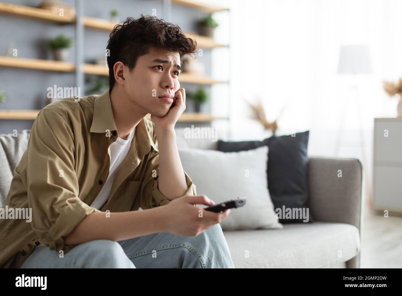 Bored asian man watching television sitting on couch Stock Photo