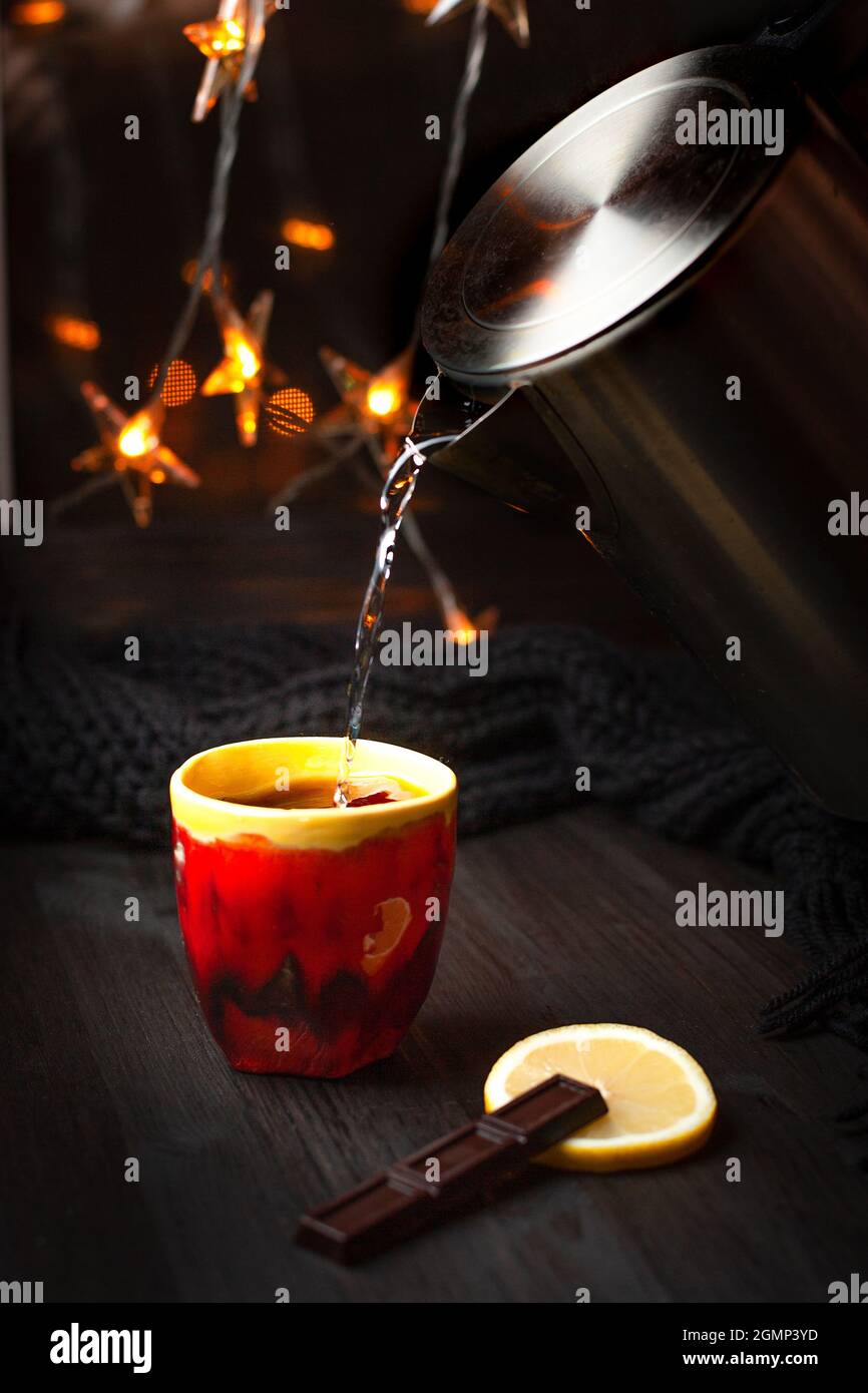 A cup of tea with lemon and chocolate on a dark background with Christmas lights. A cup of tea poured from A cup of tea poured from electric kettle Stock Photo