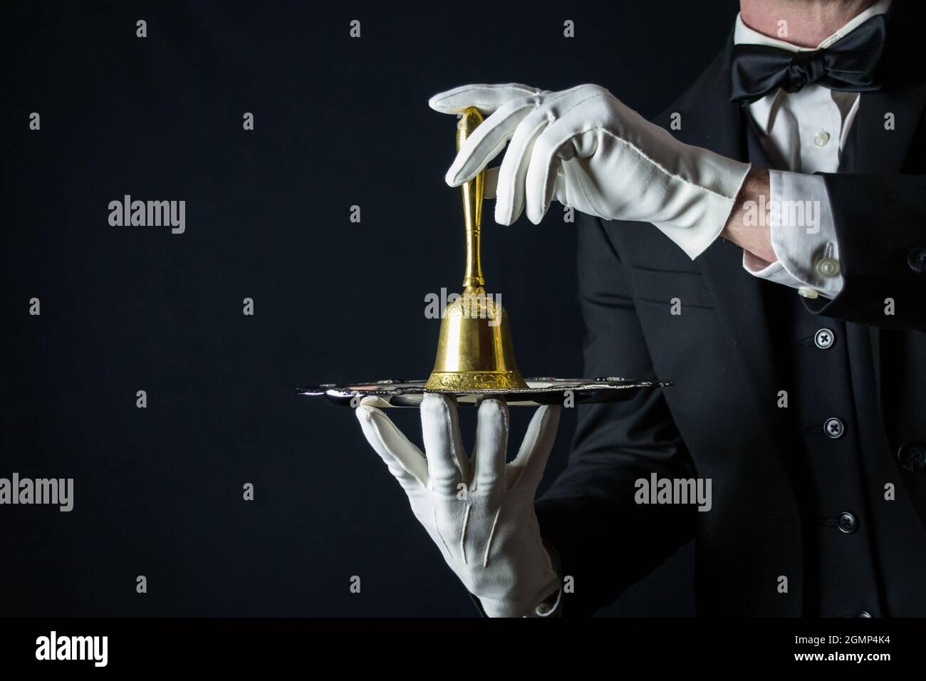 Butler or Waiter in Dark Suit and White Gloves Holding Gold Bell on Silver Tray. Concept of Service Industry and Professional Hospitality. Stock Photo