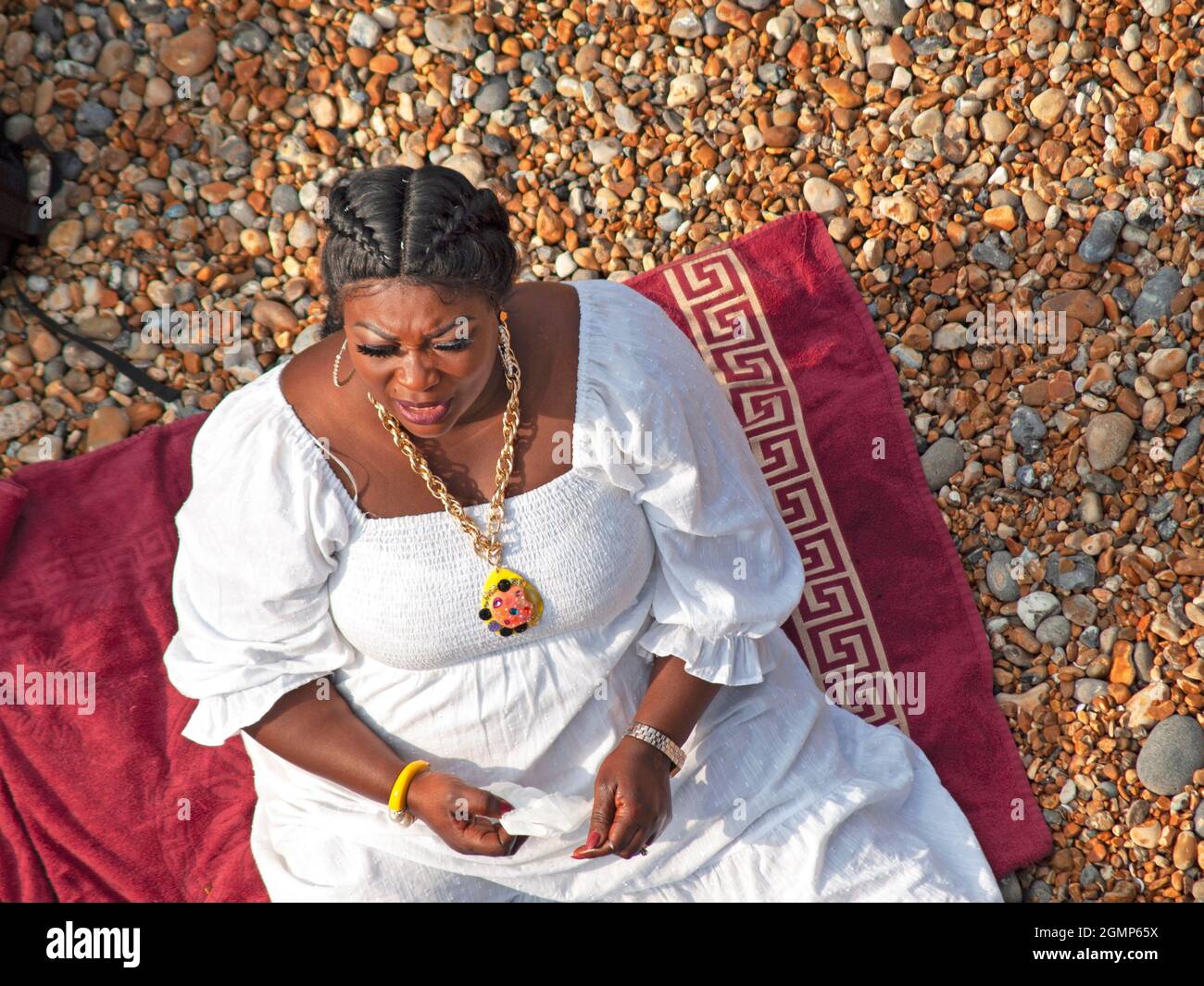 Wearing a white dress a woman sits on the beach at Brighton Stock Photo ...