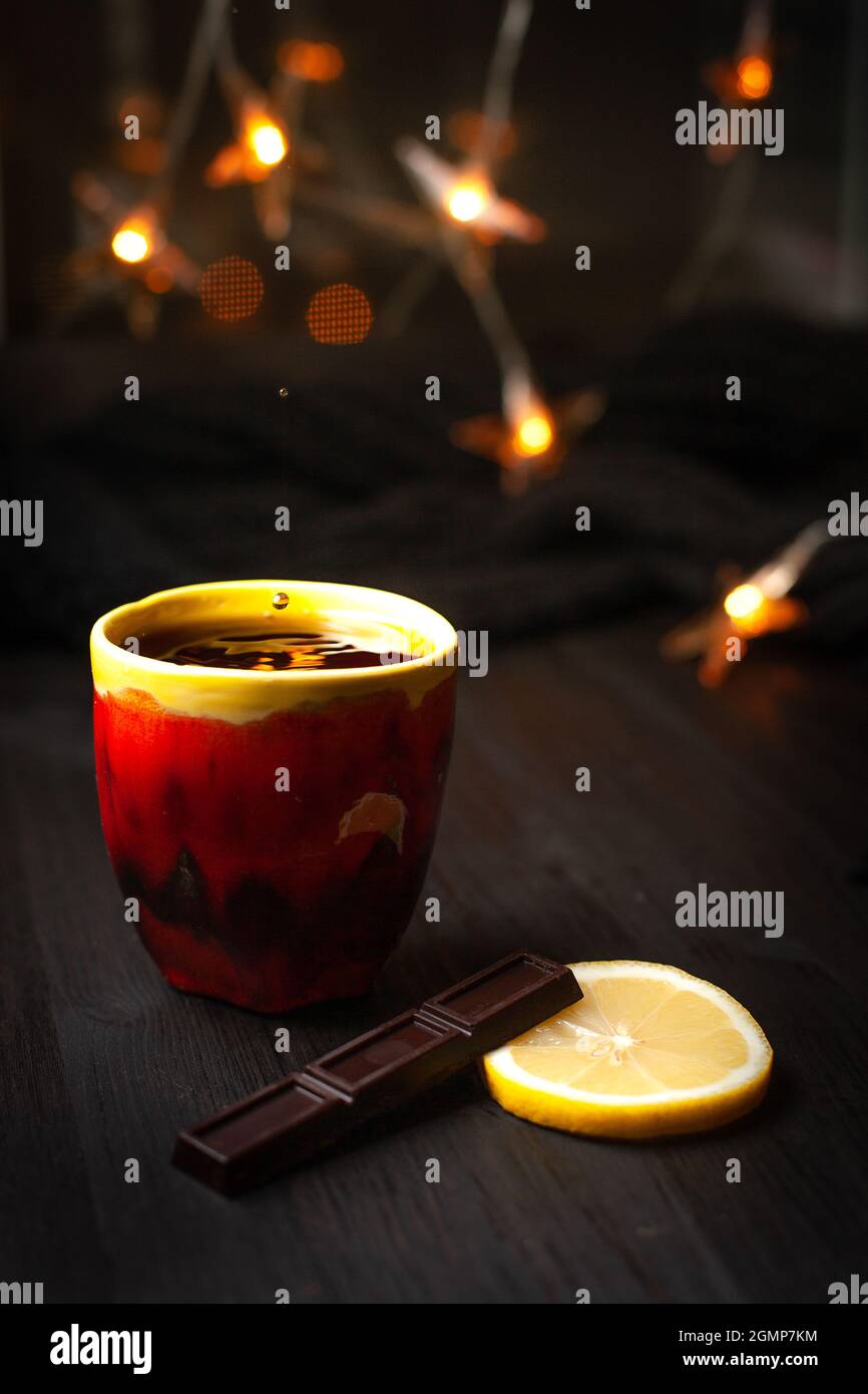 A cup of tea with lemon and chocolate on a dark background with Christmas lights Stock Photo