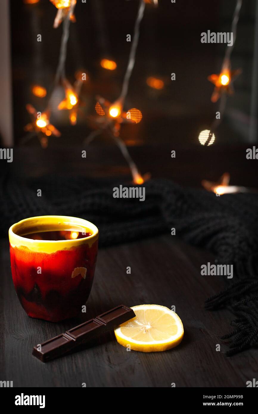 A mug of tea with slice of lemon and dark chocolate on a background with Christmas lights Stock Photo