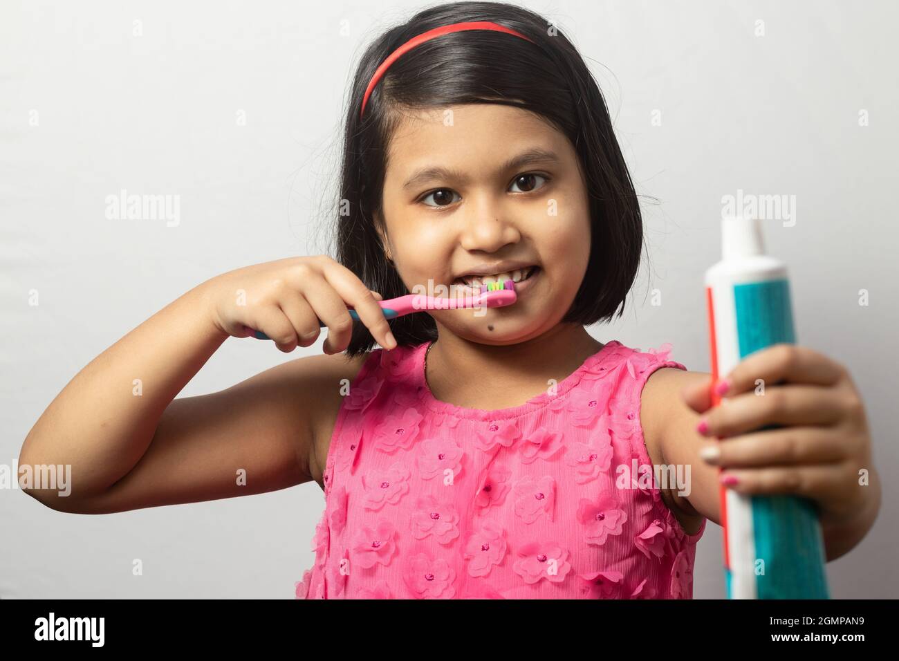 Portrait of an Indian girl child brushing teeth with toothbrush and holding toothpaste tube on