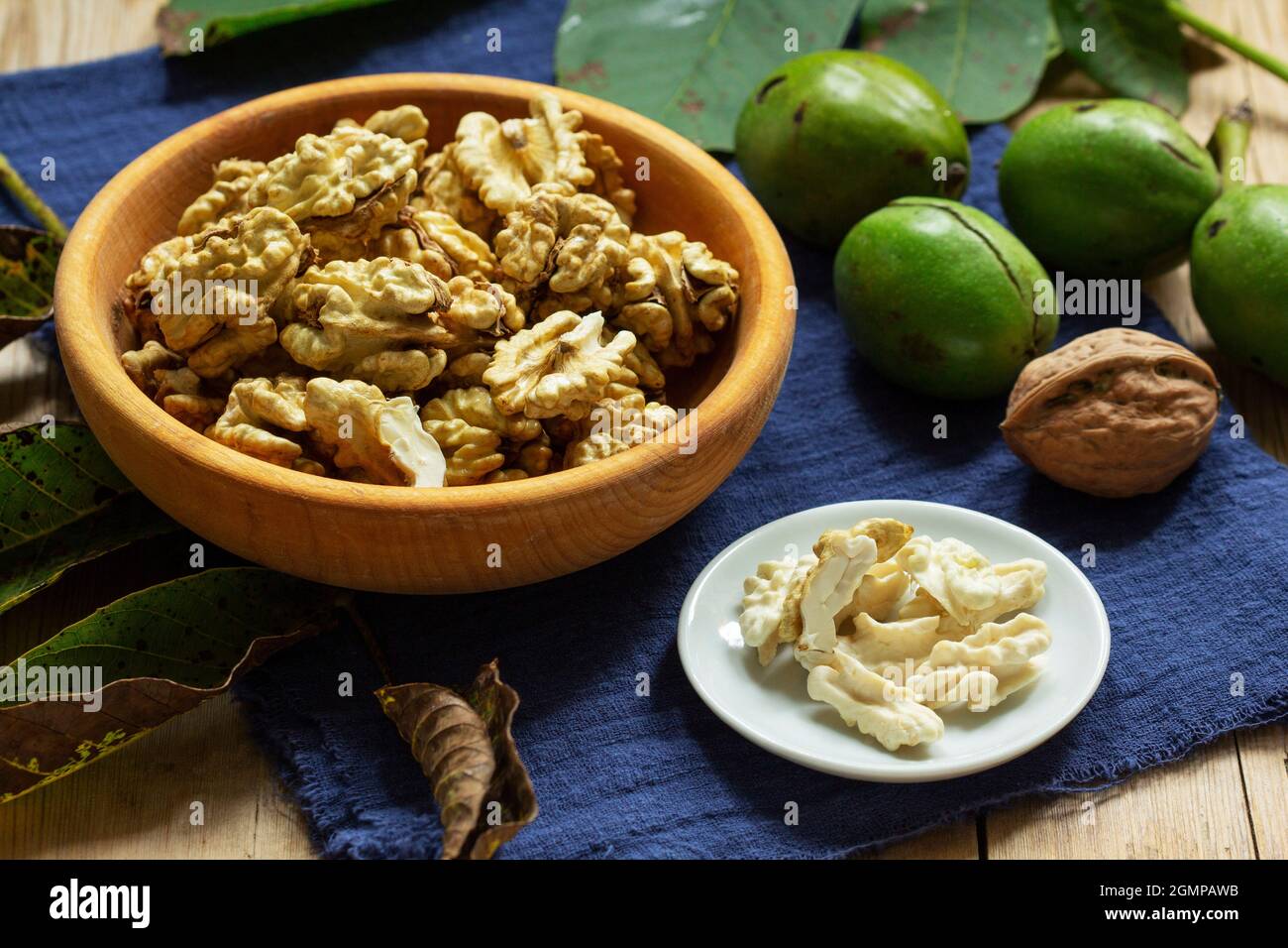 Young walnuts, shelled and in shell, walnut leaves. Rustic style. Stock Photo