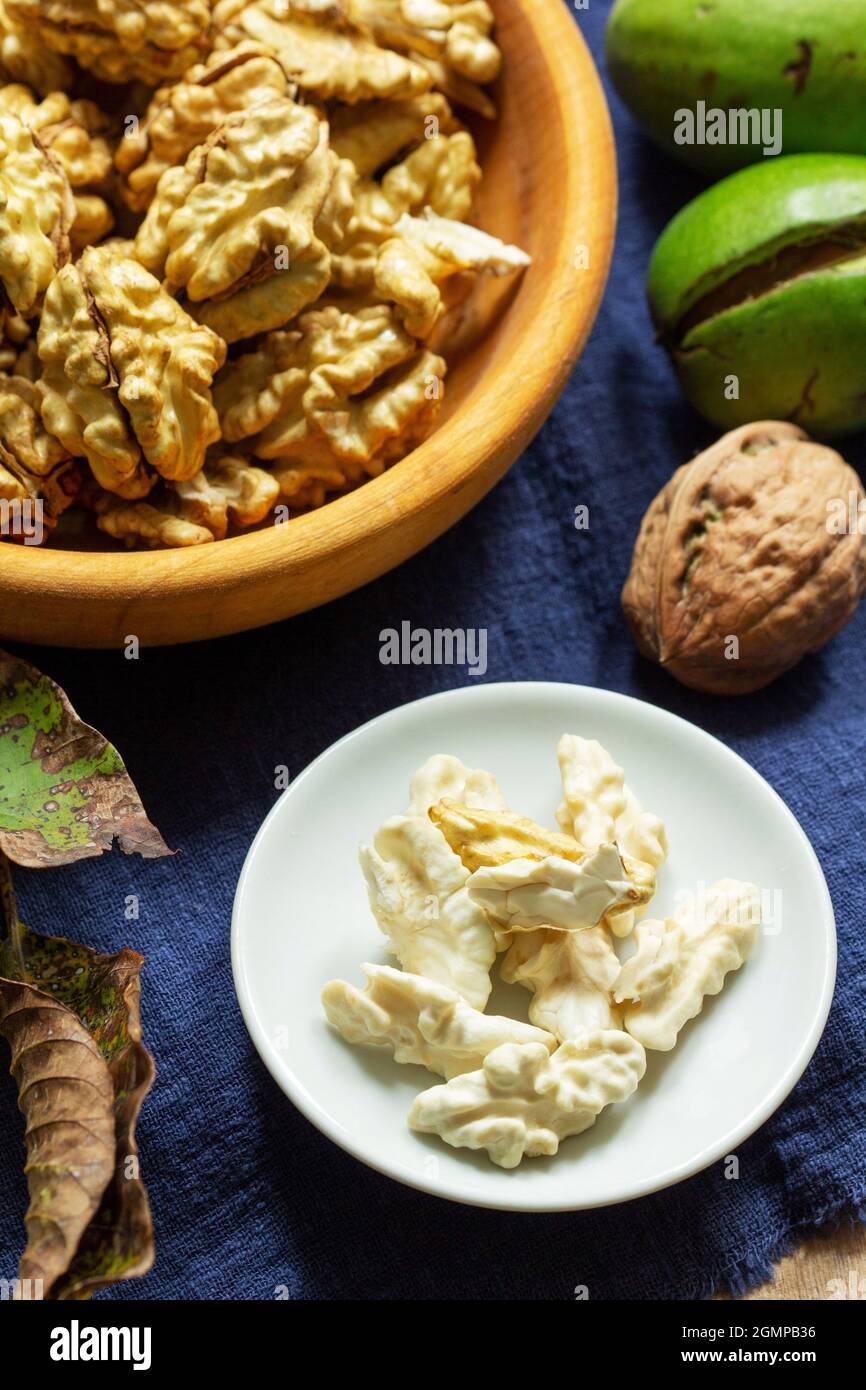 Young walnuts, shelled and in shell, walnut leaves. Rustic style. Stock Photo