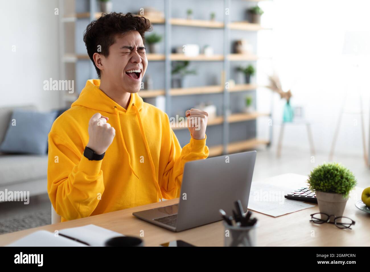 Asian man using laptop celebrating success shaking fists screaming yes Stock Photo