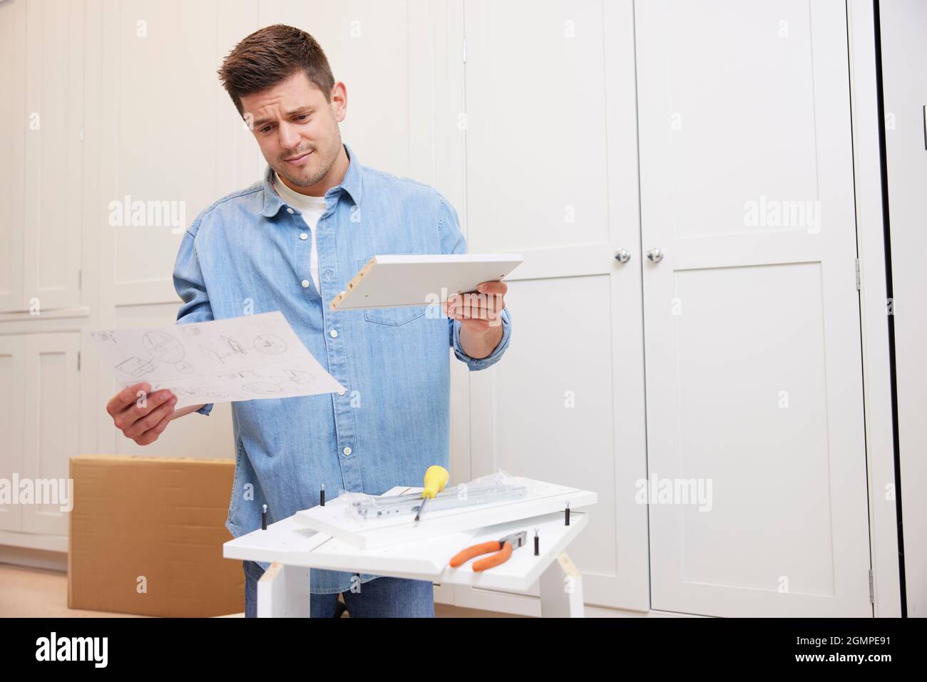 Frustrated And Confused Man Reading Instructions And Putting Together Self Assembly Furniture At Home Stock Photo