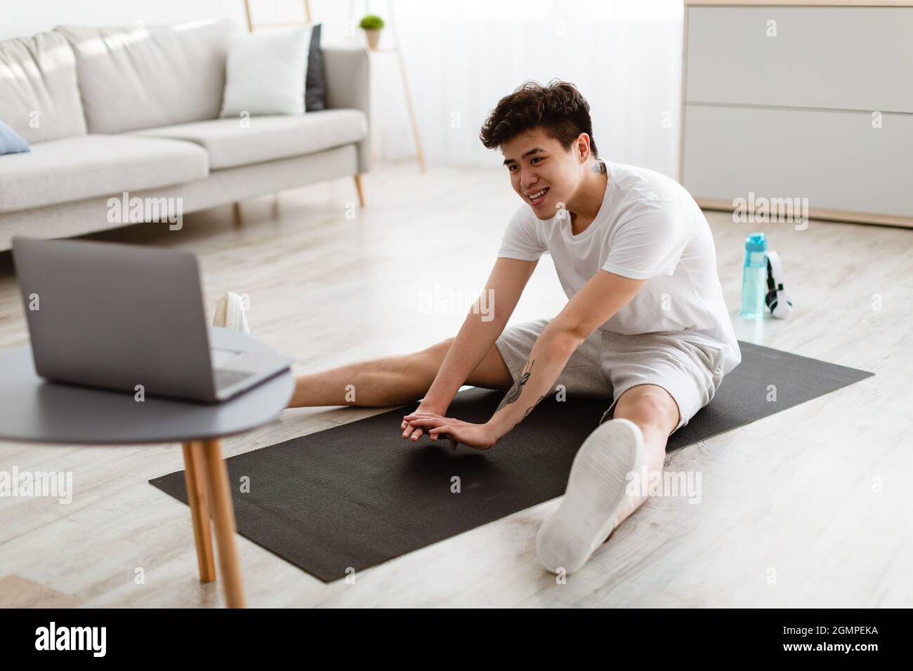 Asian guy doing stretching exercise using laptop Stock Photo