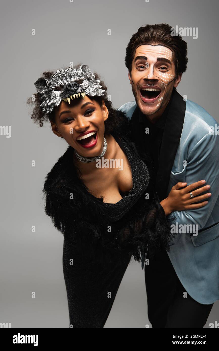 excited interracial couple in halloween costumes embracing and laughing at  camera isolated on grey Stock Photo - Alamy