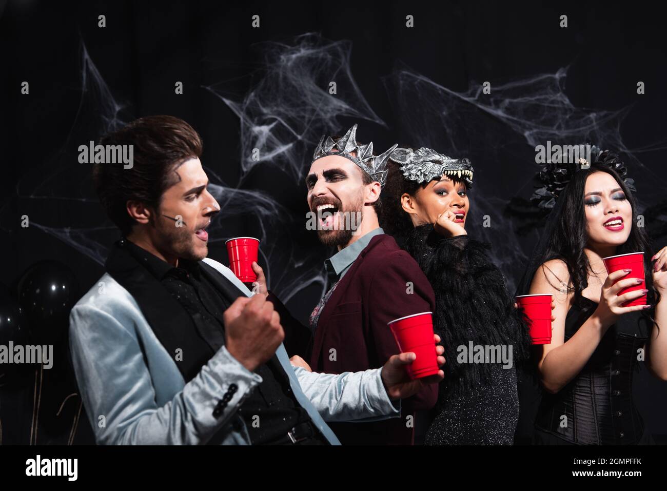 joyful multiethnic friends with plastic cups dancing on halloween party on black Stock Photo