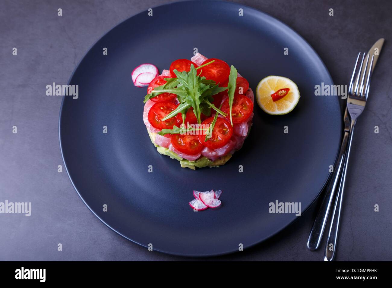 Fresh tuna tartare with avocado, arugula, cherry tomatoes, radish, chili and lime. Traditional cold appetizer of French cuisine. Close-up. Stock Photo