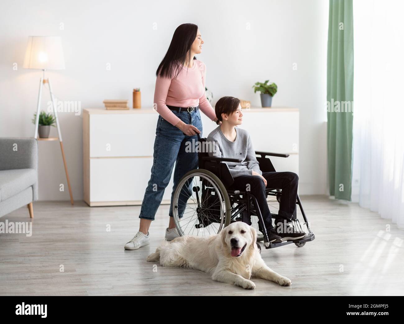 Full length of disabled teen boy with his mother and cute dog spending time together at home Stock Photo