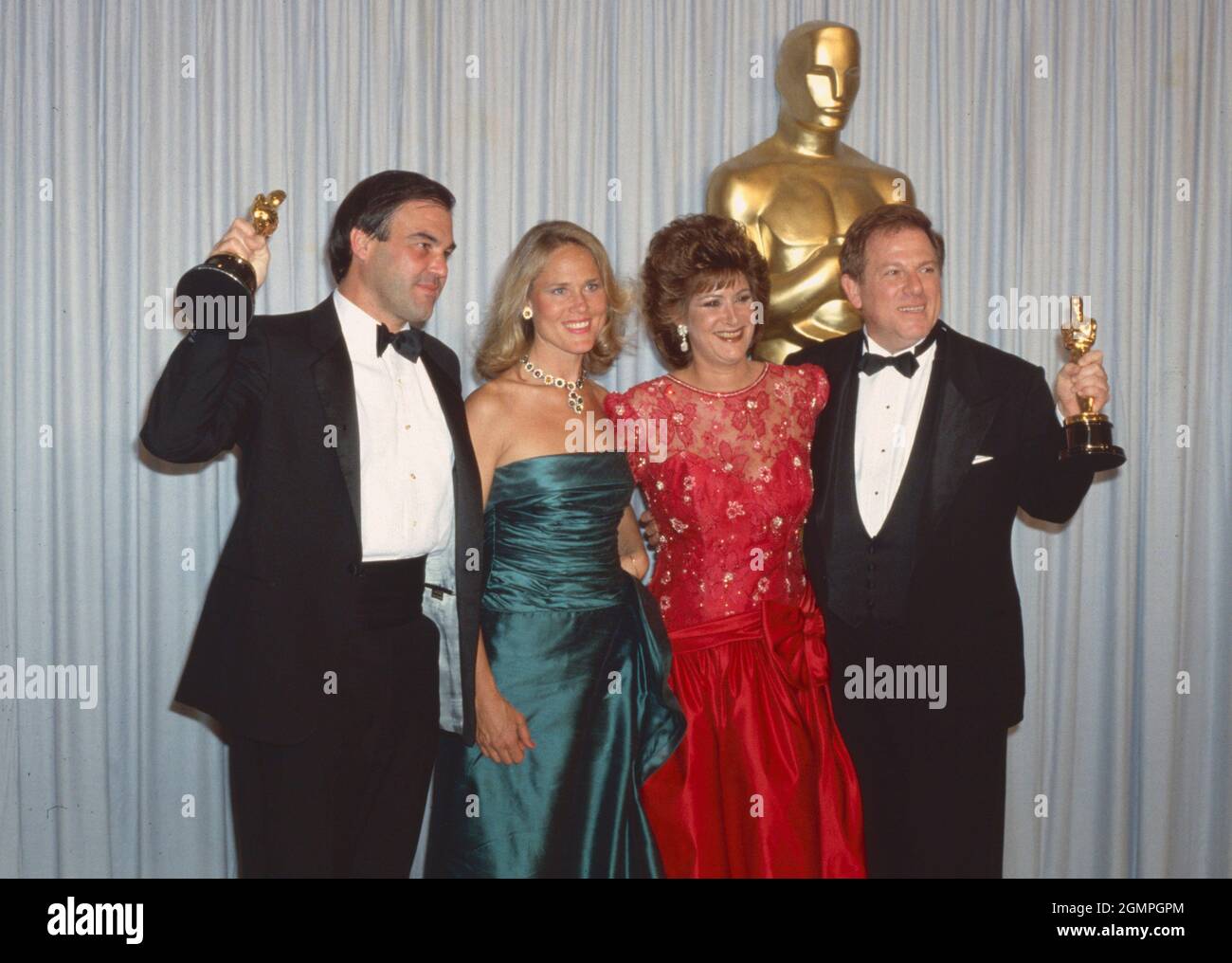 Los Angeles.CA.USA. LIBRARY. Oliver Stone and Arnold Kopelson with their  wives Elizabeth Burkit Cox (left) and Anne Feinberg (right) as their  husbands win Oscars for Platoon. 30th March 1987. UPDATED:11.09.2021  Ref:LMK30-SLIB110921PBOR-001 Peter
