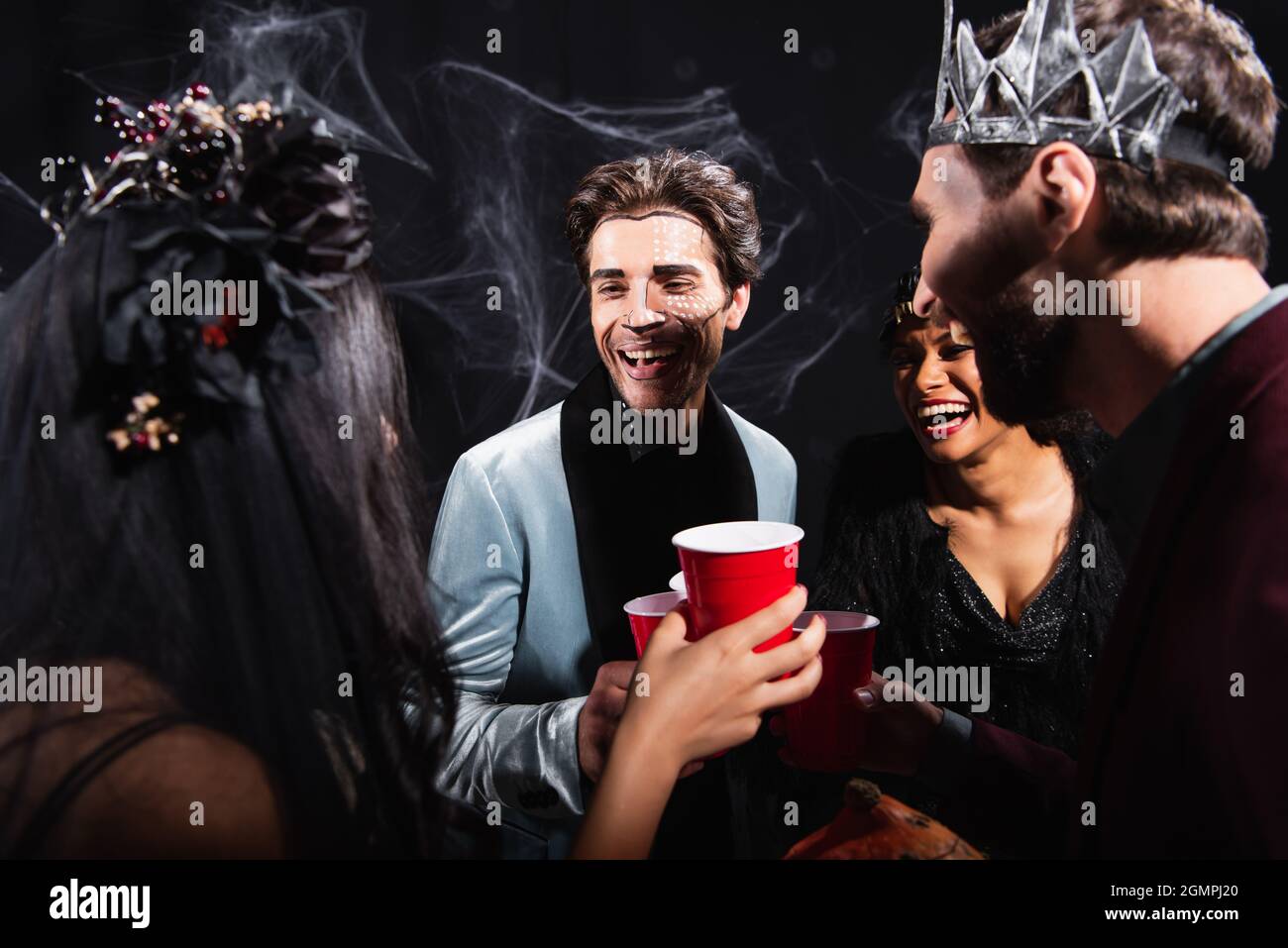 happy interracial friends in halloween makeup toasting with plastic cups on black Stock Photo