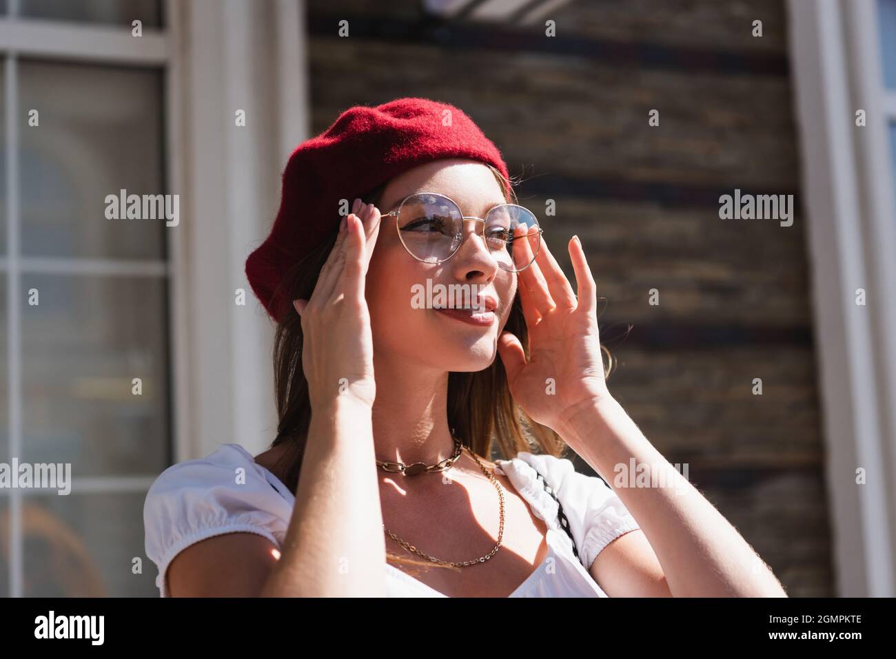 young woman in beret smiling while adjusting eyeglasses Stock Photo