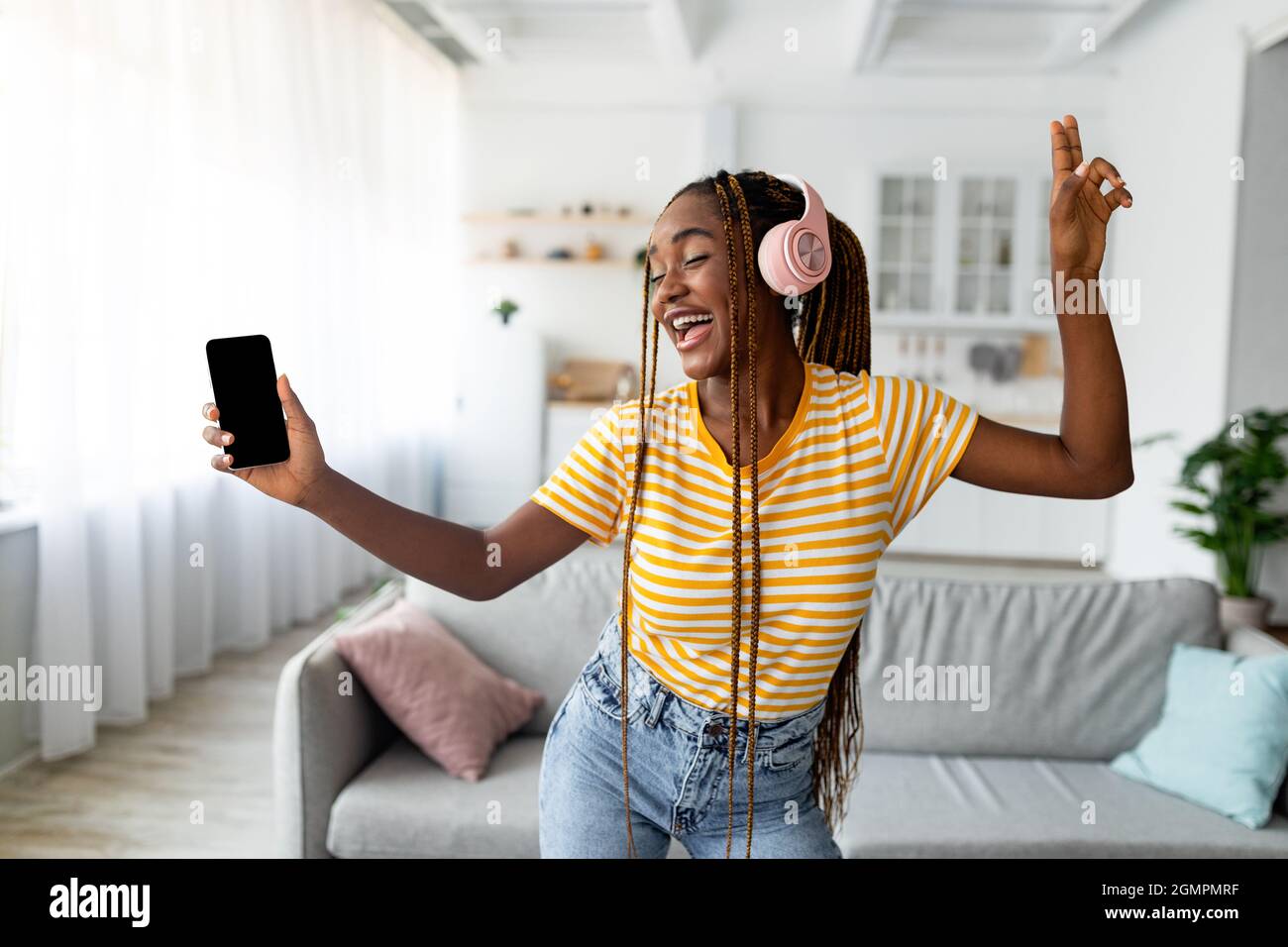 Joyful afro american long-haired woman singing and dancing, using smartphone Stock Photo