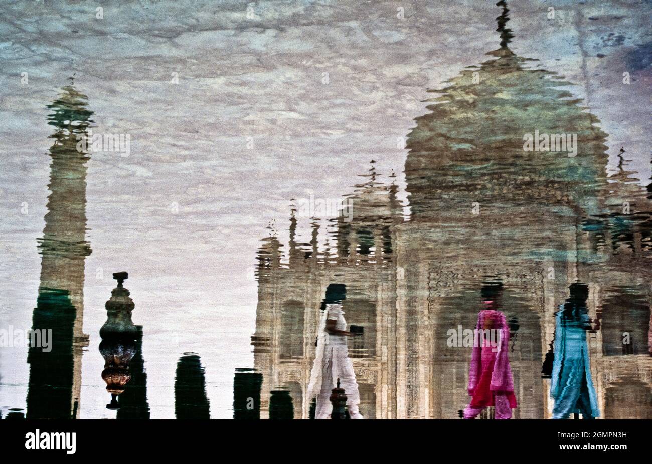 Three women wearing colorful saris are reflected in the pool in front of the Taj Mahal. Agra, Uttar Pradesh, India. Stock Photo