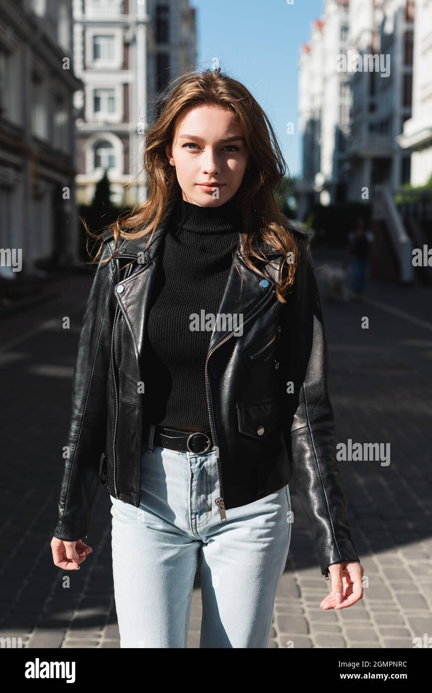 young woman in black turtleneck and leather jacket looking at camera on  urban street of europe Stock Photo - Alamy