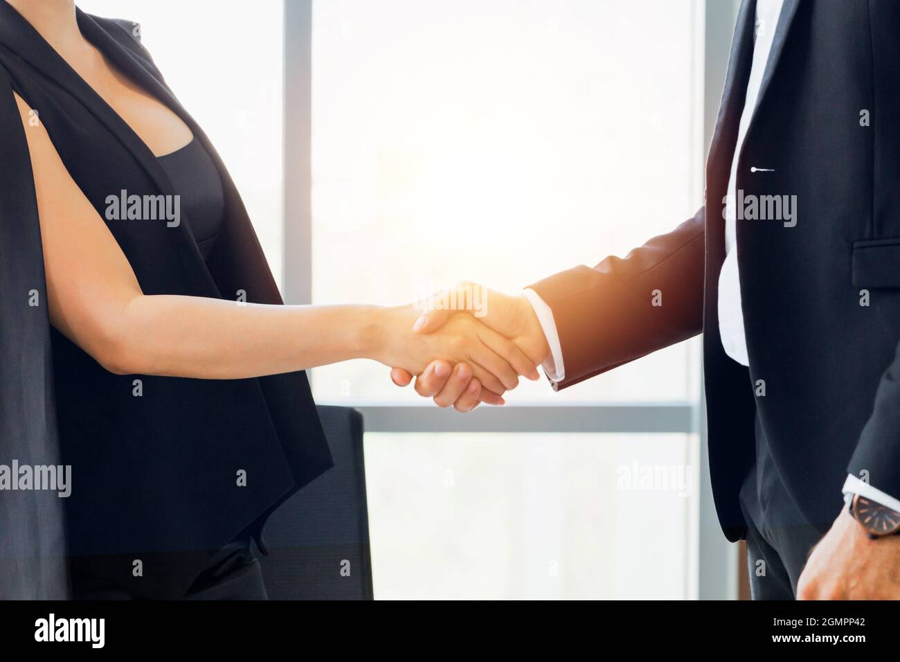 Close-up of businessman shaking hands together with business woman in indoor office environment - business greeting, success, teamwork concept Stock Photo