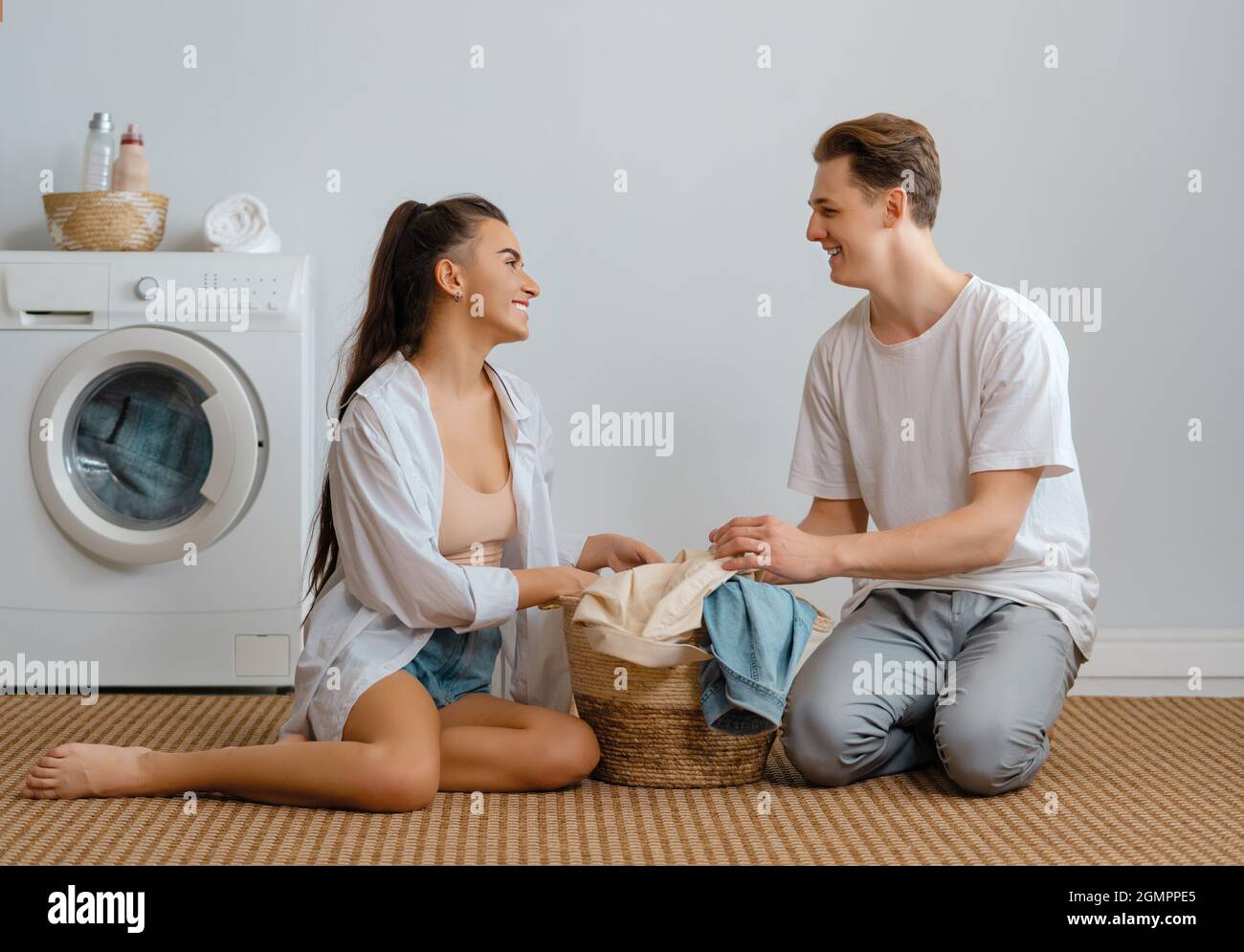 Beautiful young loving couple is smiling while doing laundry at home ...